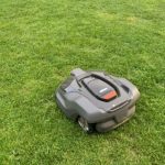 SOU's new, automated mower resembles a small Roomba vacuum sitting on grass.
