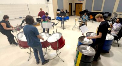 Eight musicians play a variety of percussion instruments in a circle