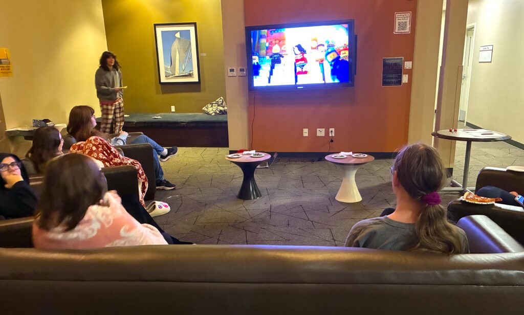 Students sit in college dorm lobby while The Lego Movie plays on a wall-mounted television
