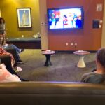 Students sit in college dorm lobby while The Lego Movie plays on a wall-mounted television