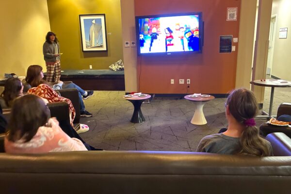 Students sit in college dorm lobby while The Lego Movie plays on a wall-mounted television